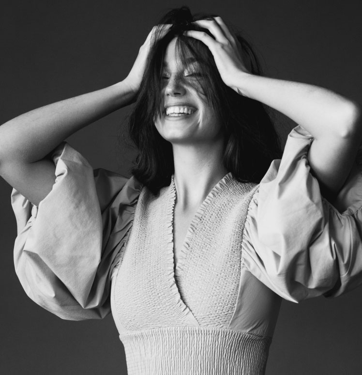A black and white image of a woman smiling with her hands on her head