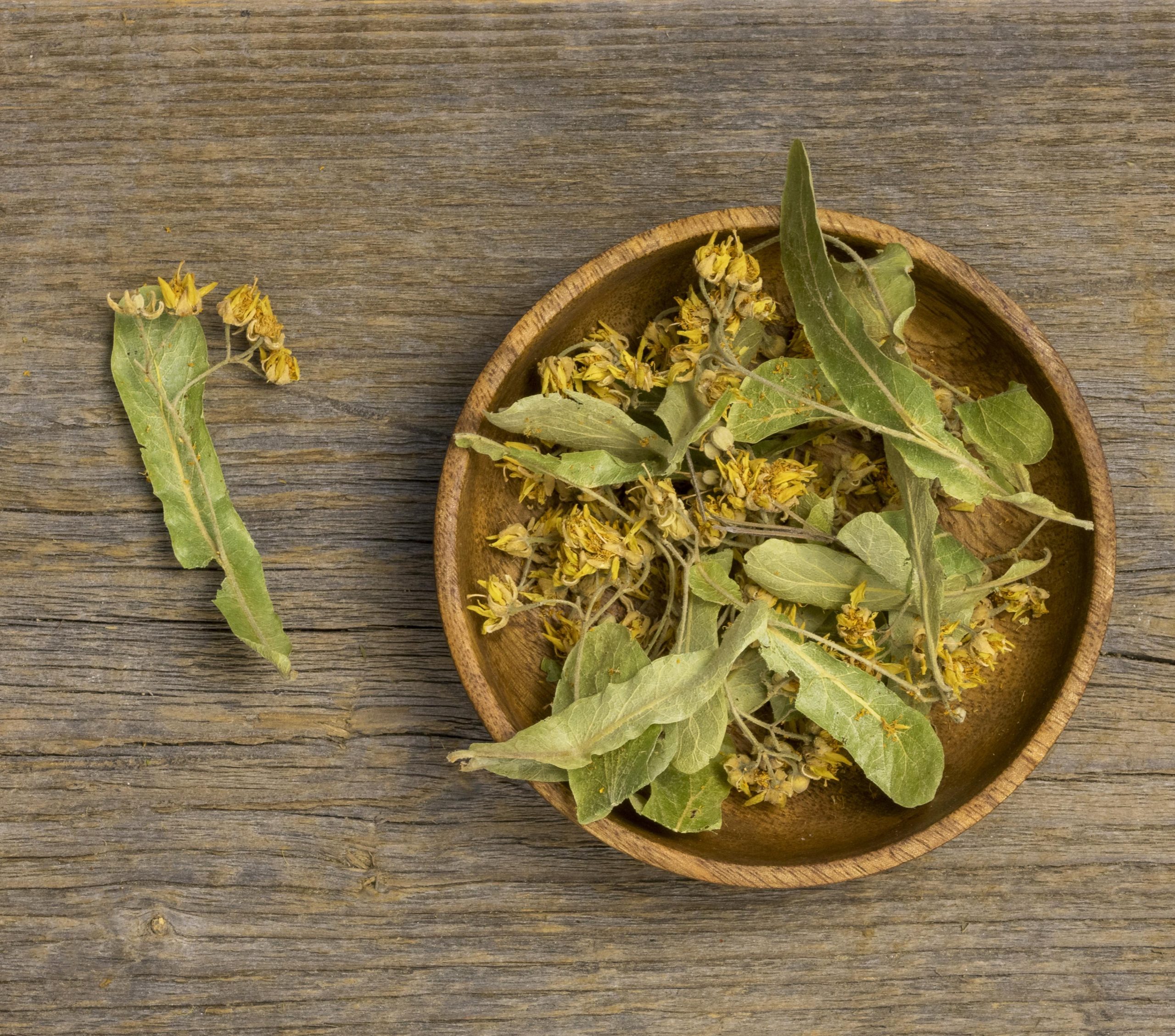 a brown bowl containing hypericum flowers and leaves that are a commonly used homeopathic remedy for nerve pain